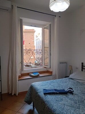 A bedroom with a bed, a window with a view of buildings, a radiator, and a curtain. - Rome: House in the heart of the 'Roman Empire (Roma)