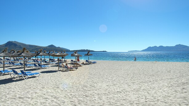 A beach with sun loungers and umbrellas, a clear sky, and mountains in the background. - VILLA MARIA - RUSTIC STAY (Pollensa)