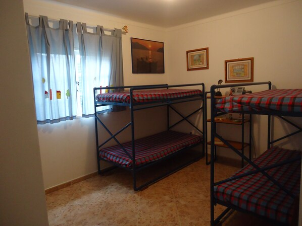 Una habitación con literas, una ventana con cortinas y dos cuadros en la pared.