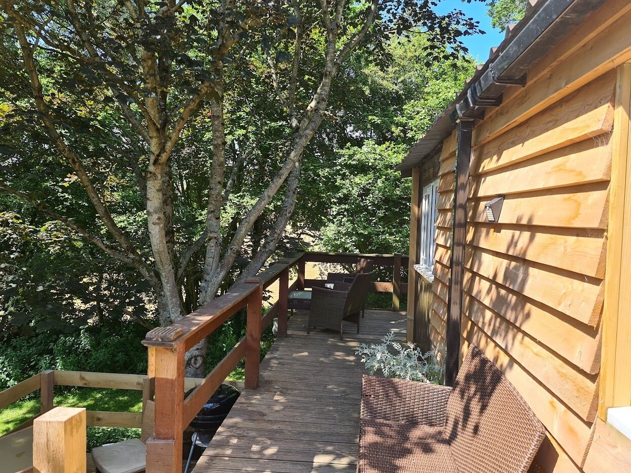 Una terraza de madera que conduce a una cabaña con baranda de madera y un banco.
