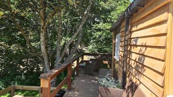 Una terraza de madera que conduce a una cabaña con baranda de madera y un banco.