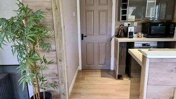 A compact kitchen with a microwave, kettle, and cabinets. A bamboo plant is in a pot near the entrance.