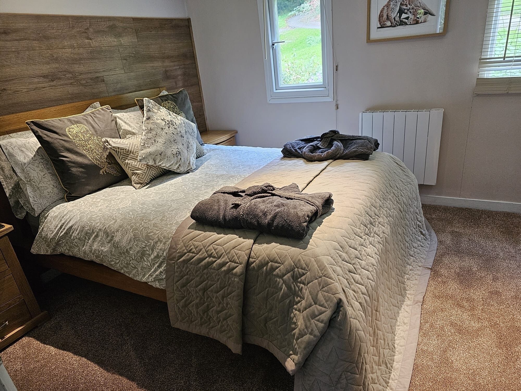 Une chambre à coucher avec un lit, des oreillers, une couverture matelassée, un radiateur et une fenêtre donnant sur un paysage verdoyant.