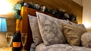 Un lit avec une tête de lit en bois, une bouteille de Canti Prosecco et deux verres posés sur une table de chevet en bois.
