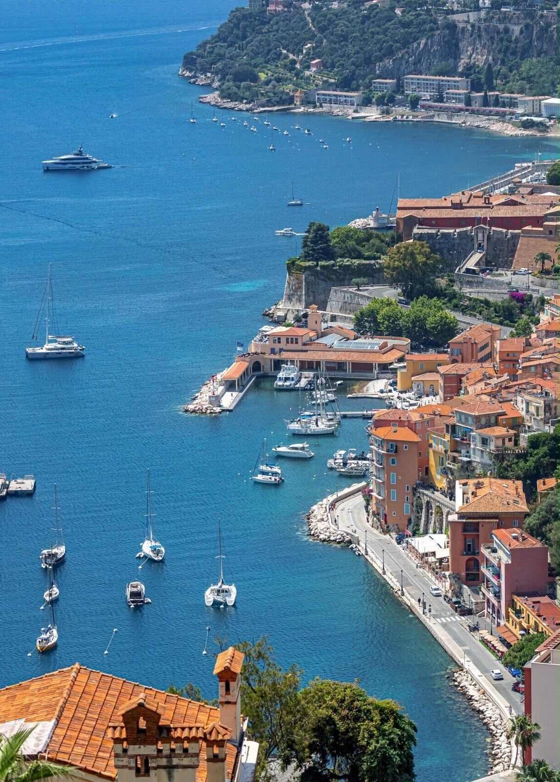 Una cittadina costiera con un porto turistico, edifici con tetti in tegole rosse e un mare cristallino.
