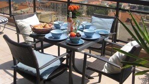 Mesa de varanda com pratos, tigelas e garrafa azuis, com vista para um porto cheio de barcos.