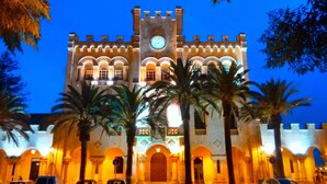 A historic building with a clock tower, arched windows, and palm trees in the foreground. - Villa with private pool,  at 150 m of the beach (Ciutadella de Menorca)