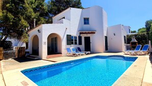 A poolside area with a clear blue pool, two lounge chairs, and a white building with a tiled roof. - Villa with private pool,  at 150 m of the beach (Ciutadella de Menorca)
