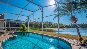 A swimming pool with a clear view of a lake and palm trees, enclosed by a glass structure. - SOUTHFACING  Private Pool, Lakeview,4 BR-2 Bath,Ultra Clean Modern,10 min Disney (Kissimmee)