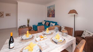 A dining area with a table set for four, a bottle of wine, and a painting on the wall. - Walk to Beach & Strip Stylish 2BR w/ Pool, Terrace & BBQ | Albufeira (Albufeira)