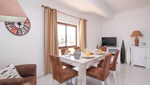 A dining area with a white table, brown chairs, and a television in the background. - Walk to Beach & Strip Stylish 2BR w/ Pool, Terrace & BBQ | Albufeira (Albufeira)