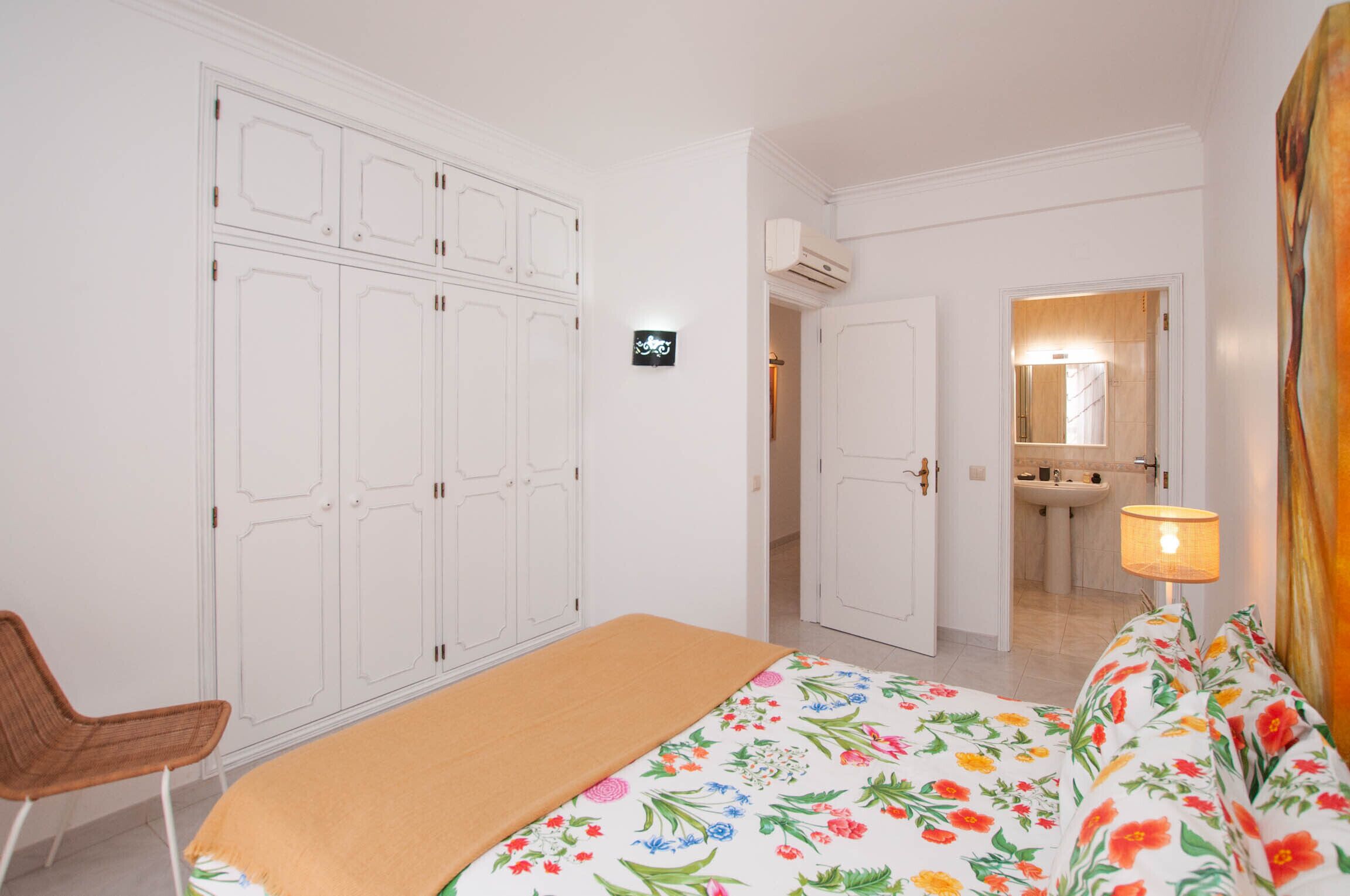 A bedroom with a bed, a chair, a wardrobe, and a bathroom visible through an open door.
