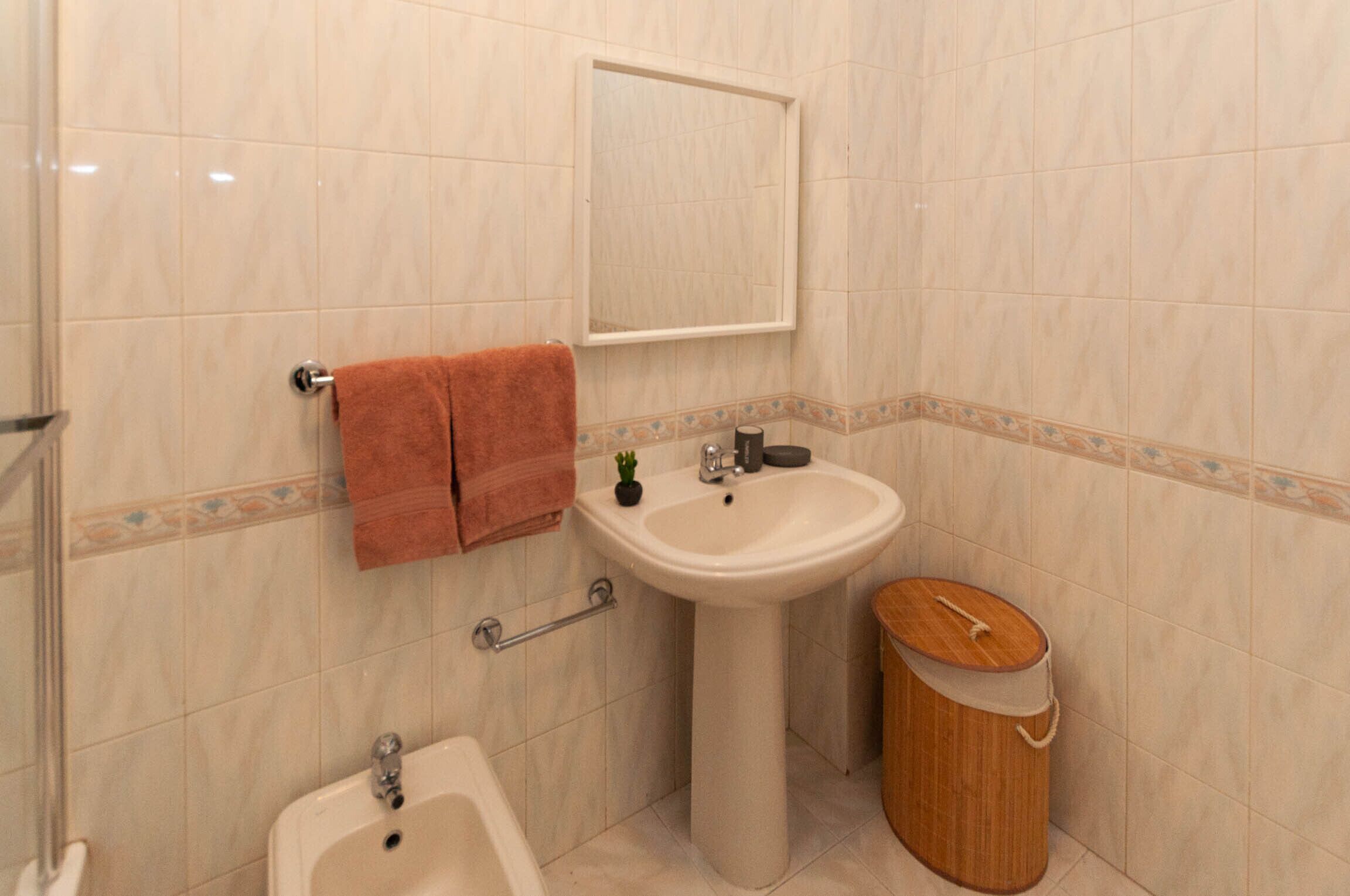 Une salle de bain équipée d’un lavabo, d’un miroir, d’un porte-serviettes et d’un seau en bois.