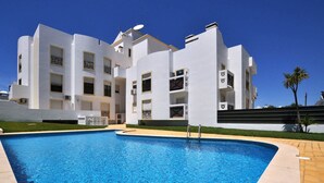 A modern building with a swimming pool, featuring multiple balconies and a clear blue sky. - Walk to Beach & Strip Stylish 2BR w/ Pool, Terrace & BBQ | Albufeira (Albufeira)