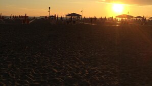 A beach at sunset with a clear sky, a sun low on the horizon, and beachgoers in the distance. - Villa (Pieve Camaiore)