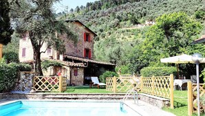 A stone building with a red window, a swimming pool, and a wooden fence. - Villa (Pieve Camaiore)