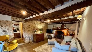 A cozy living room with a stone wall, wooden beams, a fireplace, a TV, and a bar area. - Villa (Pieve Camaiore)