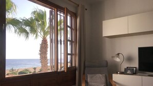 A room with a large window overlooking a beach, a chair, a desk with a lamp, and a television. - Vacation rental (vv) In Puerto Del Carmen, Lanzarote, Canary Islands (Puerto Del Carmen)