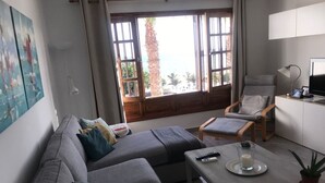 A living room with a gray sofa, a coffee table with a remote control, a chair, and a TV on a stand. - Vacation rental (vv) In Puerto Del Carmen, Lanzarote, Canary Islands (Puerto Del Carmen)