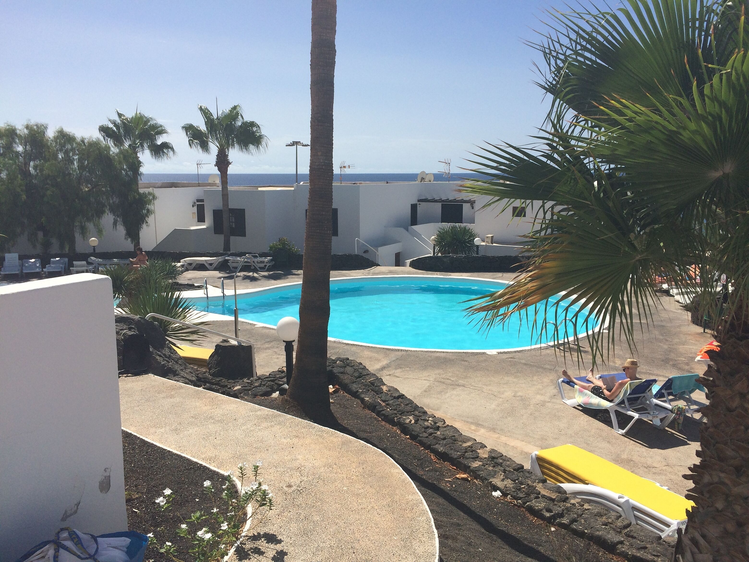 A pool area with lounge chairs and palm trees, surrounded by buildings.