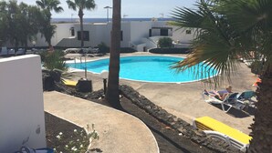 A pool area with lounge chairs and palm trees, surrounded by buildings. - Vacation rental (vv) In Puerto Del Carmen, Lanzarote, Canary Islands (Puerto Del Carmen)