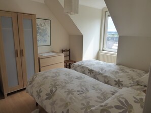 A bedroom with two beds, a wooden wardrobe, a desk, and a window with a view.