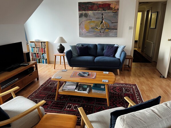 A living room with a sofa, coffee table, TV, bookshelf, and a painting on the wall.