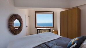 A bedroom with a bed, a wooden wardrobe, a round mirror, and a window with a view of the sea. - Luxury villa apartment with panoramic sea views and small private garden (Nice)