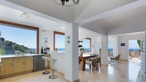 A modern kitchen with large windows, a dining area with a view, and a spacious living area. - Luxury villa apartment with panoramic sea views and small private garden (Nice)