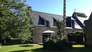 A stone house with a sloped roof, a chimney, and a small garden with a palm tree and a white umbrella. - House with large garden classified 3 stars 5 km from the sea (Concarneau)