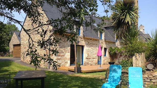 A stone house with a wooden deck, a pink umbrella, and two blue lounge chairs. - House with large garden classified 3 stars 5 km from the sea (Concarneau)