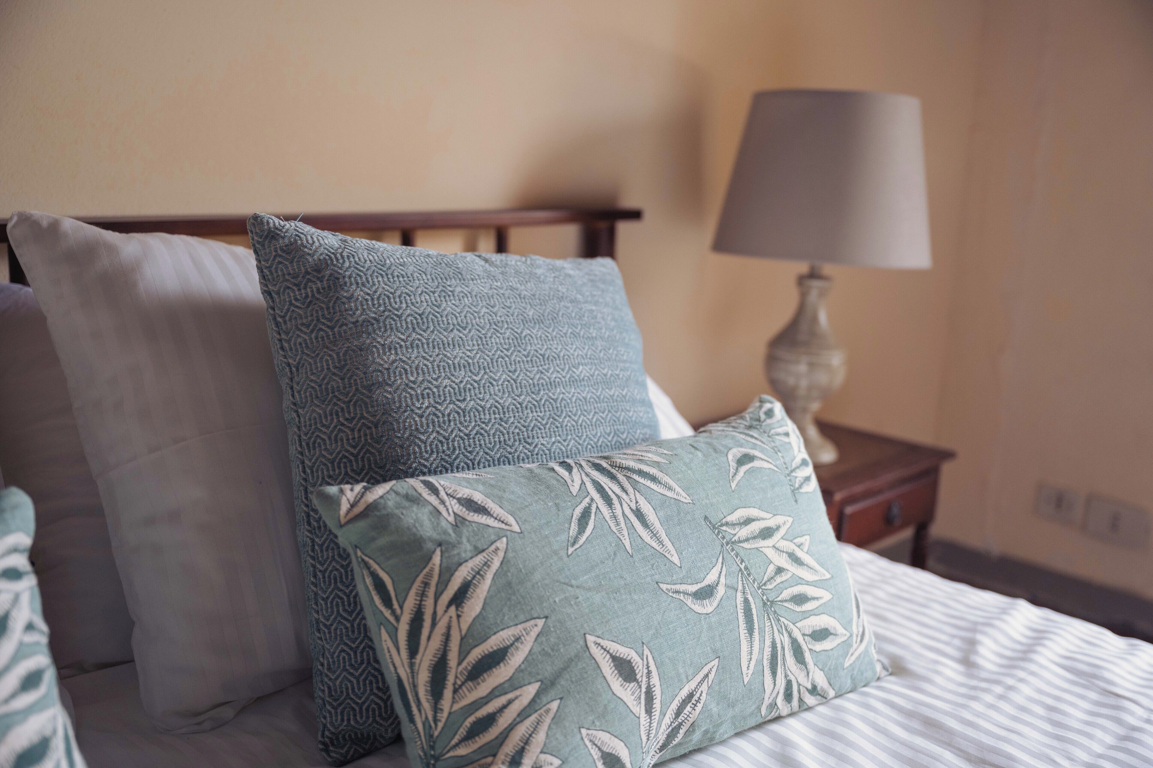 A neatly made bed with patterned pillows and a bedside table with a lamp.