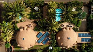 Luchtbeeld van een resort met twee grote bolvormige constructies, zonnepanelen en een zwembad omringd door palmbomen.
