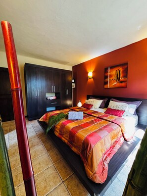 Ein Schlafzimmer mit einem Bett, einem dunklen Holzschrank, einem Gemälde an der Wand und einer roten Säule.