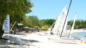 Una playa con veleros, un letrero que dice "Campsite" y un edificio al fondo.
