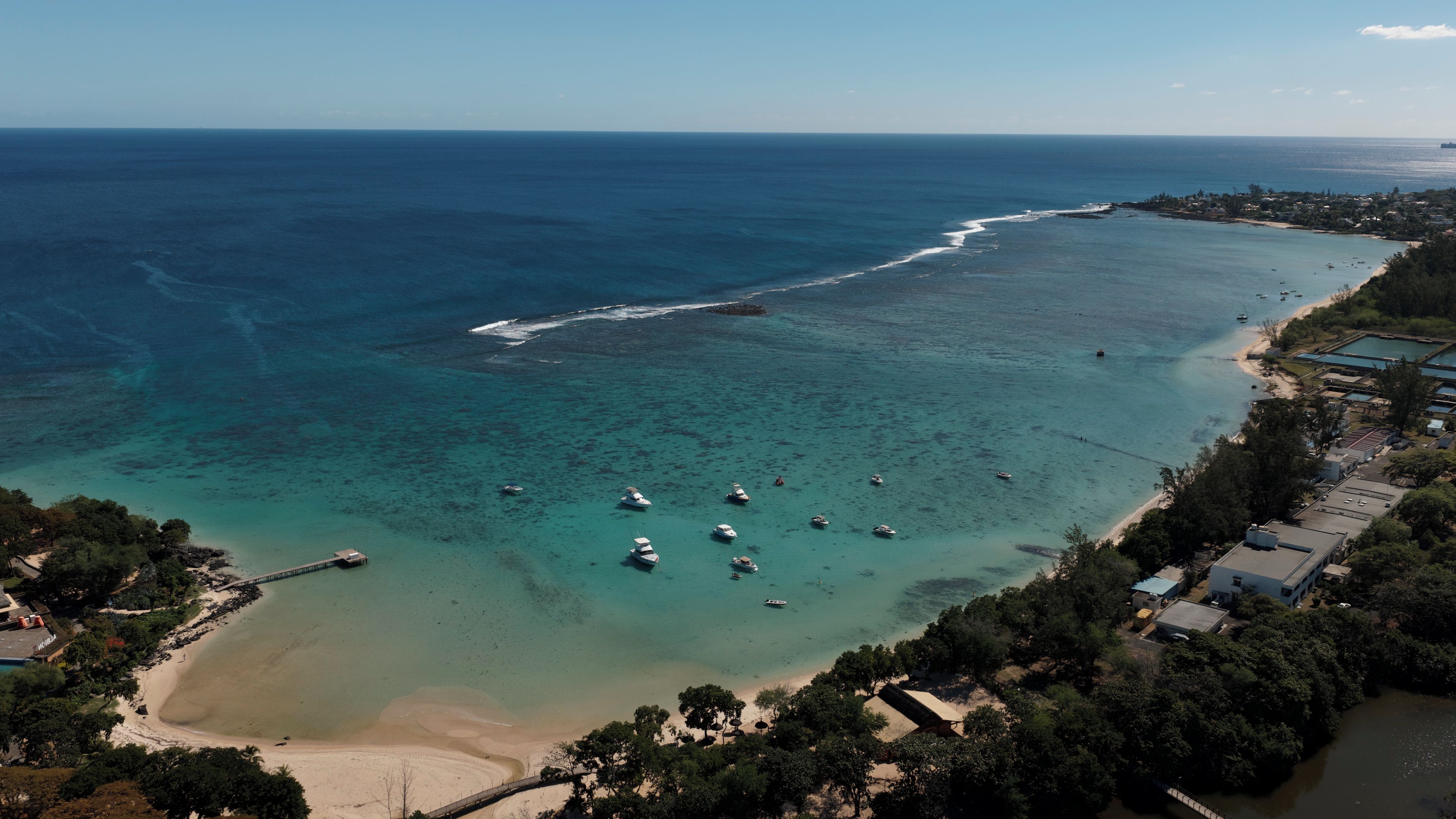 Vista aérea de una zona costera con aguas cristalinas, embarcaciones y una playa.