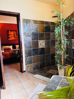 A bathroom with a shower area, a bamboo plant, and a painting on the wall.