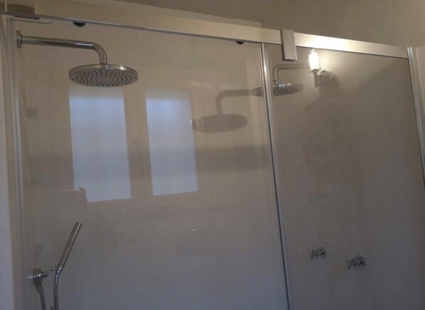 Un área de ducha con paredes de vidrio, con un cabezal de ducha de mano y otro fijo en la pared.