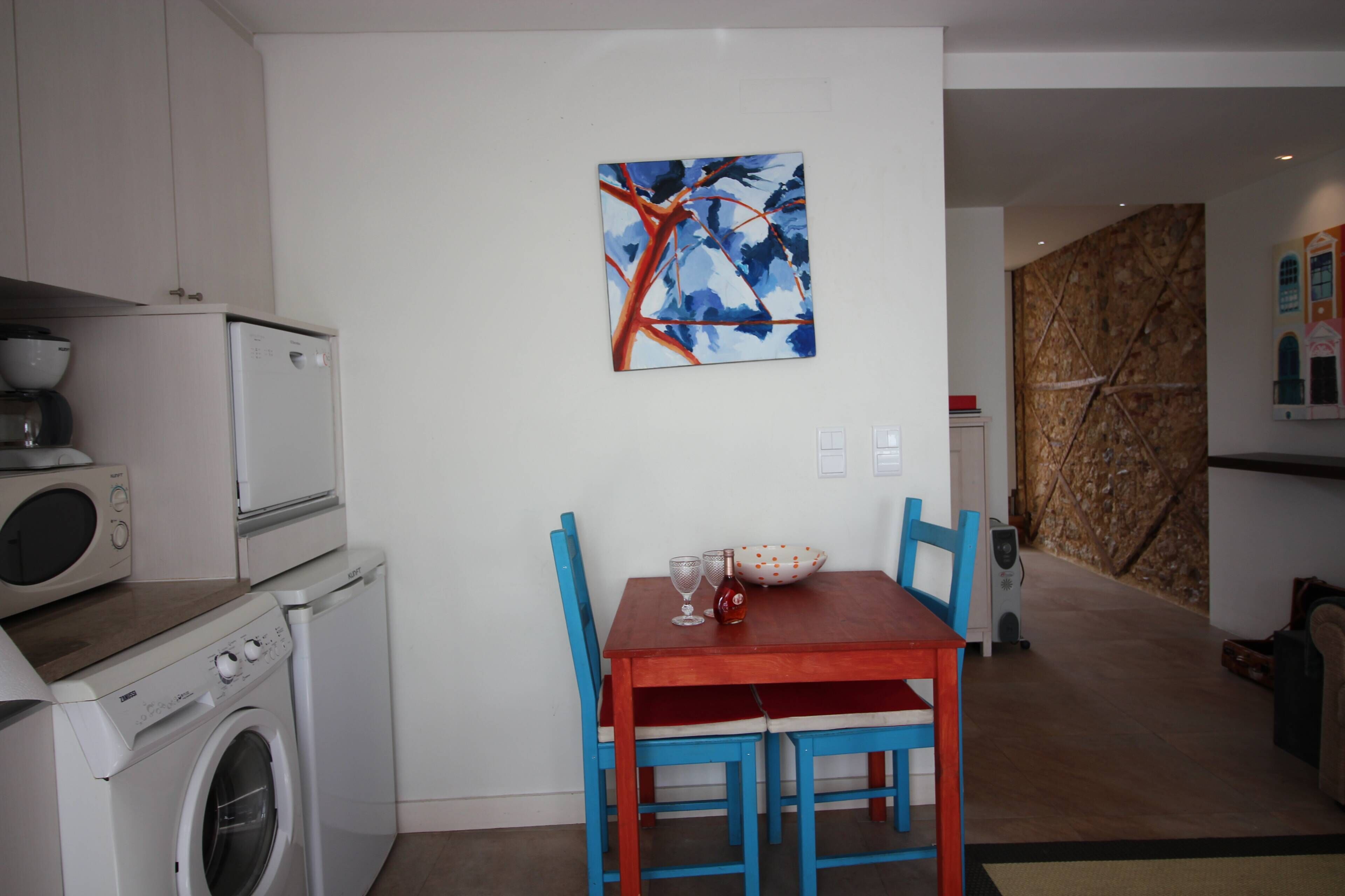 Une cuisine compacte équipée d’un lave-linge, d’une table à manger avec des chaises et d’un tableau accroché au mur.