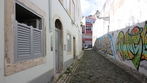 Una estrecha calle adoquinada con un edificio a la izquierda que presenta una puerta y contraventanas, y una pared llena de grafitis coloridos a la derecha.