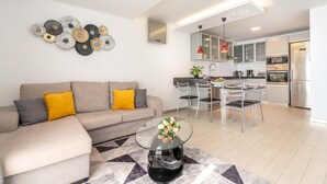 Un saló modern amb un sofà, una taula de centre de vidre i una cuina al fons.