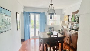 A spacious kitchen with a dining table and chairs, a hanging light fixture, and a view through the open door. - Private farm with pool in the Alentejo (Vila Nova da Baronia)