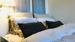 A bed with white and beige bedding, two blue doors, and a wall-mounted lamp. - Private farm with pool in the Alentejo (Vila Nova da Baronia)