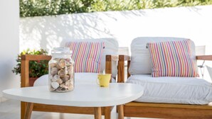 A round white table with a glass jar of seashells and a yellow cup. Two white chairs with colorful striped pillows are in the background. - Small indenpendent villa first line 50m. Air con. WIFI. Bbq. privat garden. (Dénia)