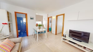 A modern living room with a flat-screen TV, a dining area with a table and chairs, and a kitchen in the background. - Small indenpendent villa first line 50m. Air con. WIFI. Bbq. privat garden. (Dénia)