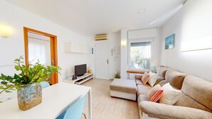 A modern living room with a sofa, a TV, a dining table, and a potted plant. - Small indenpendent villa first line 50m. Air con. WIFI. Bbq. privat garden. (Dénia)