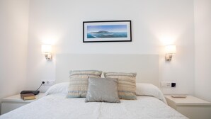 A neatly made bed with a framed picture above it, two bedside tables with lamps, and a power outlet on the wall. - Small indenpendent villa first line 50m. Air con. WIFI. Bbq. privat garden. (Dénia)