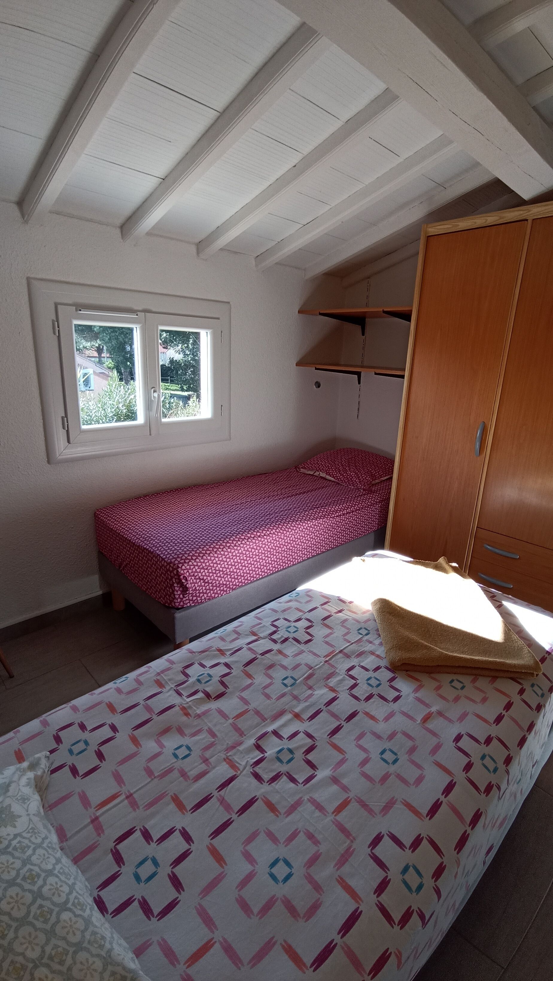 A small, single-bed room with a sloped ceiling and a window.