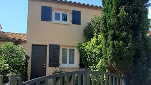 Un edificio residencial con fachada color crema, una reja oscura y un árbol alto al frente.