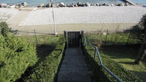Unes escales que porten a una zona de platja, amb una tanca, un fanal i un moll que s'endinsa a l'aigua.